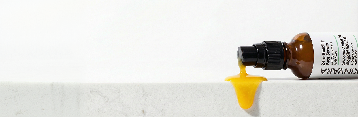 Golden rosehip serum dripping from the bottle onto marble